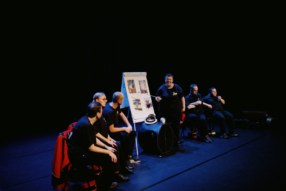 Een aantal leden van Fenix Theatermakers zitten op een stoel op het podium. Een vrouw geeft een soort presentatie met een turnover.